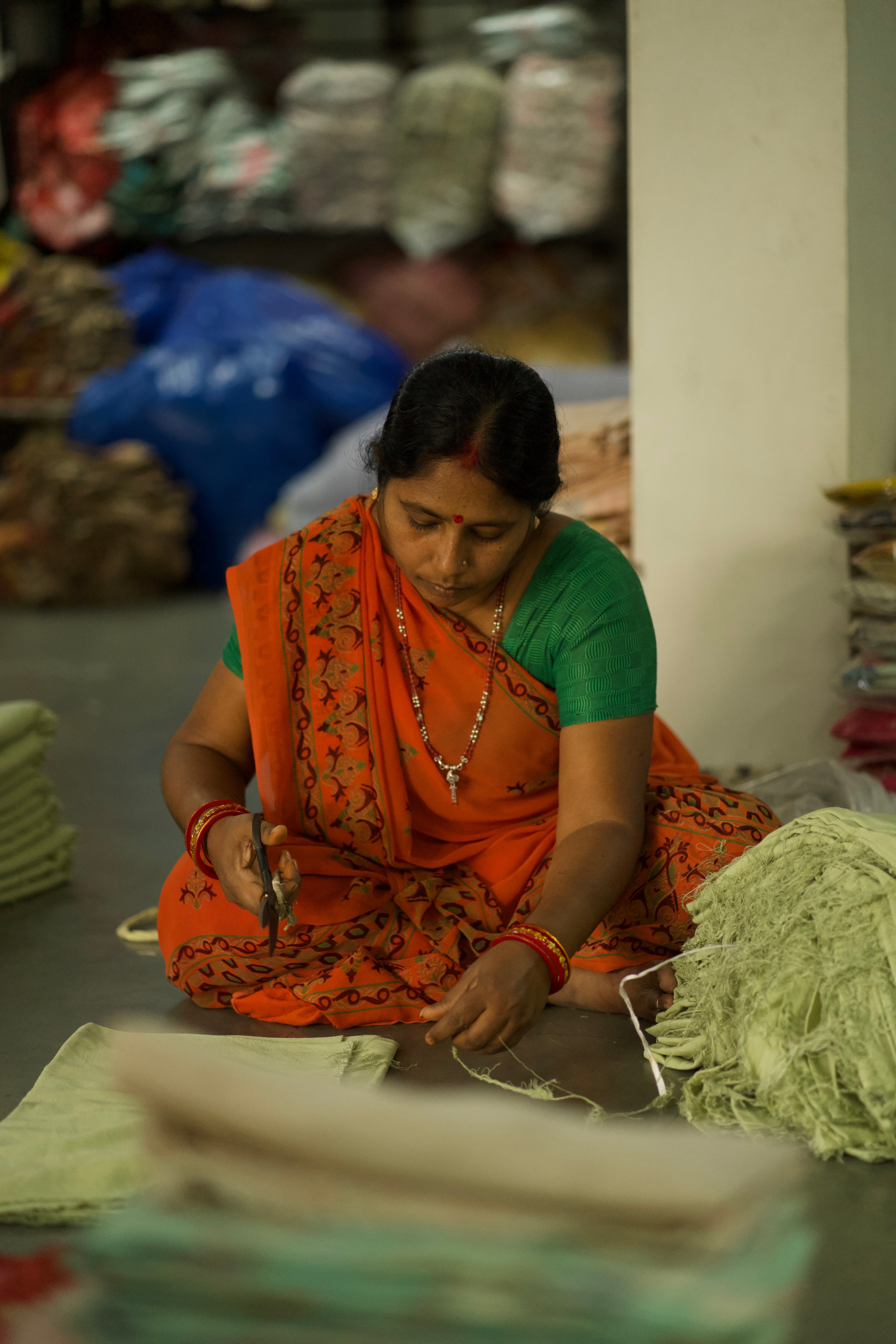 Woman in an orange saree working with fabric in a workshop setting.